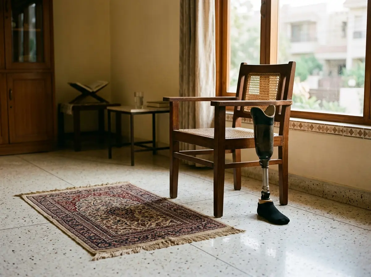 A finely woven prayer mat laid on a clean polished floor beside a simple sturdy wooden chair in a quiet sunlit room of a Karachi home, with a below knee artificial leg standing upright next to the chair. No people. Photograph taken in Karachi, Pakistan. Any person shown is Pakistani and well dressed, with the face out of frame. Natural daylight, realistic colours, documentary style. No text, no signage, no logos, no watermarks. 4:3 aspect ratio.